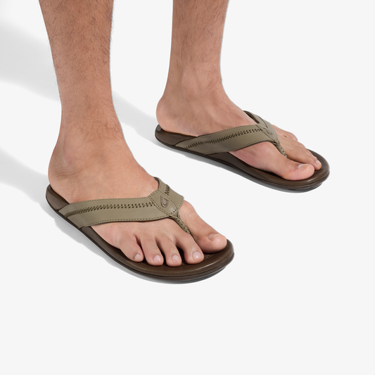 Tan and brown thong sandals with stitched straps worn on feet against white background.