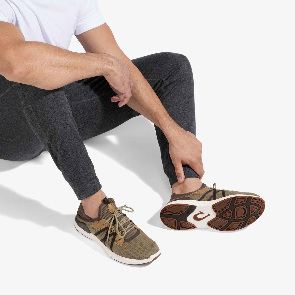 Man wearing dark gray leggings and tan/brown lace-up sneaker with white sole, shown from waist down.