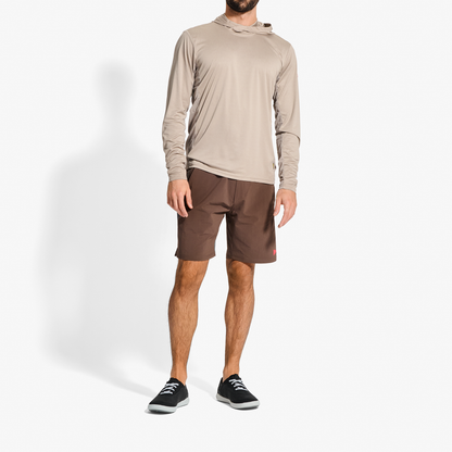 Man wearing beige hooded long-sleeve shirt and brown shorts with black and white sneakers.