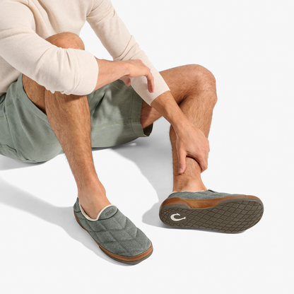 Man wearing ash-colored quilted slippers with brown sole, paired with sage shorts and cream long-sleeve shirt.