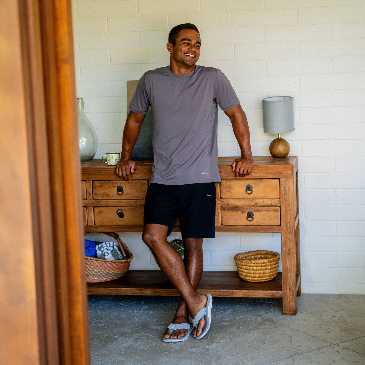 Man wearing ash gray short-sleeve t-shirt and black shorts with light blue slide sandals.