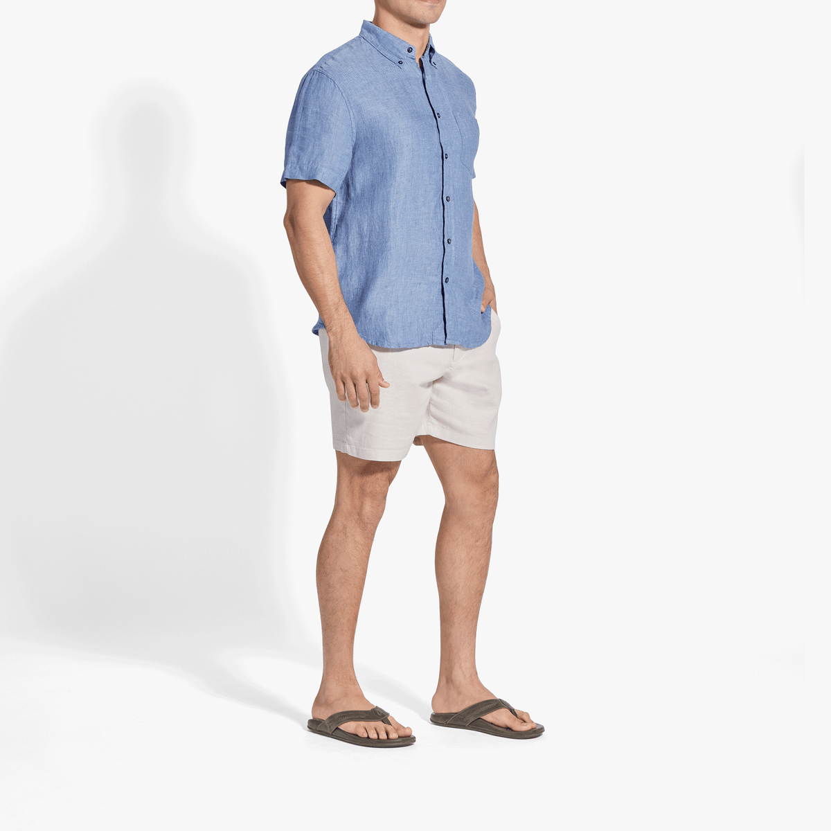 Man wearing blue short-sleeve button-up shirt with white shorts and dark sandals.