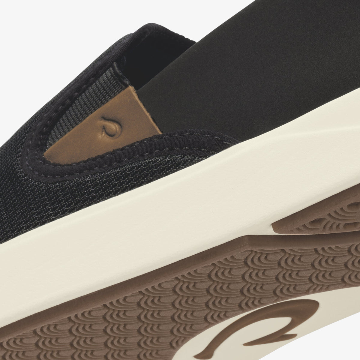 Black slip-on shoe with tan heel patch and cream and brown patterned sole.
