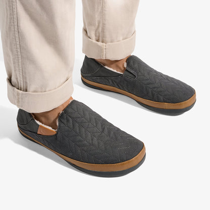 Dark gray quilted slip-on slippers with tan rubber soles, worn with rolled cream pants.