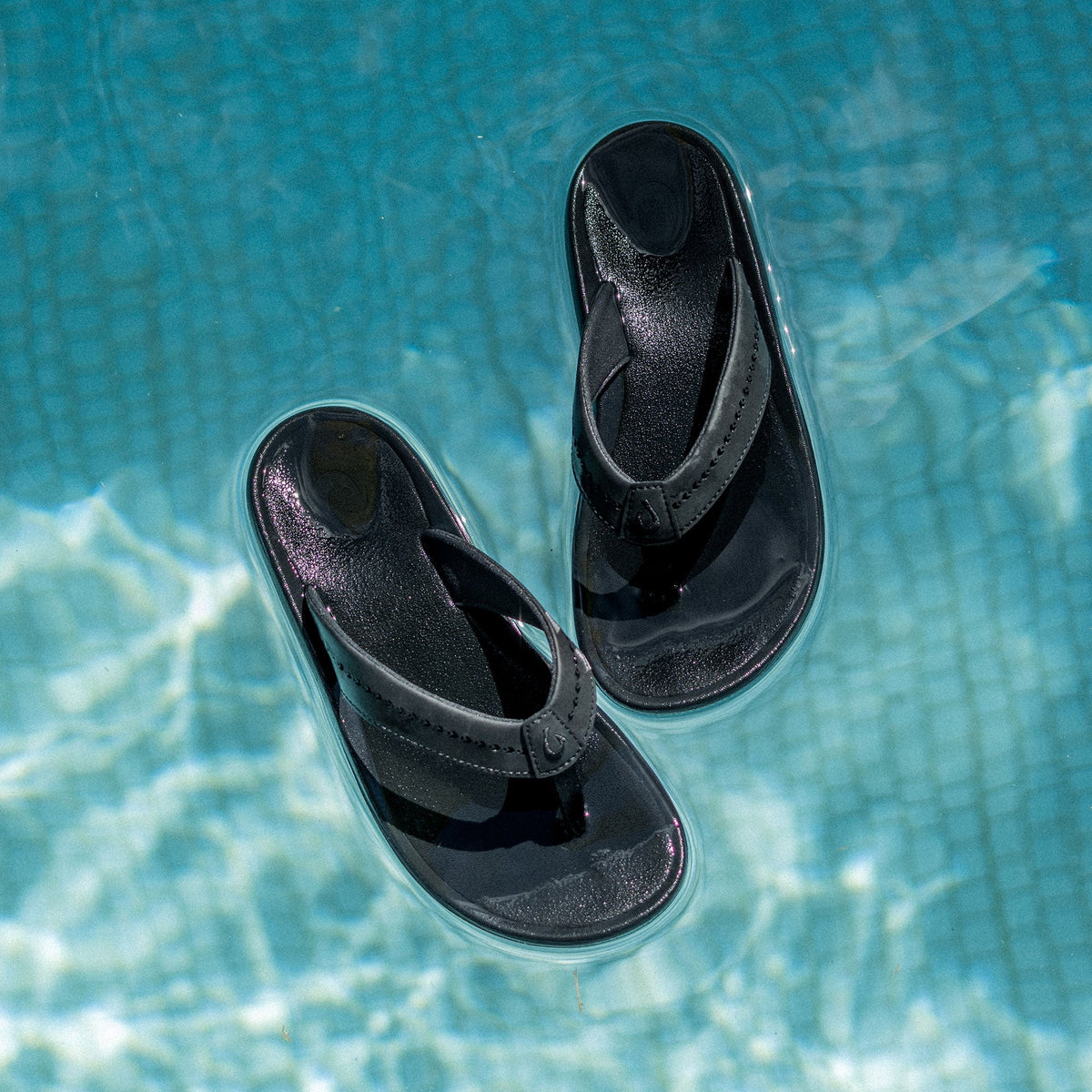 Black flip-flop sandals with textured footbeds and curved straps, shown floating on water surface.