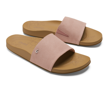 Pair of slide sandals with soft pink suede uppers and warm sand-colored rubber soles featuring embossed floral design.