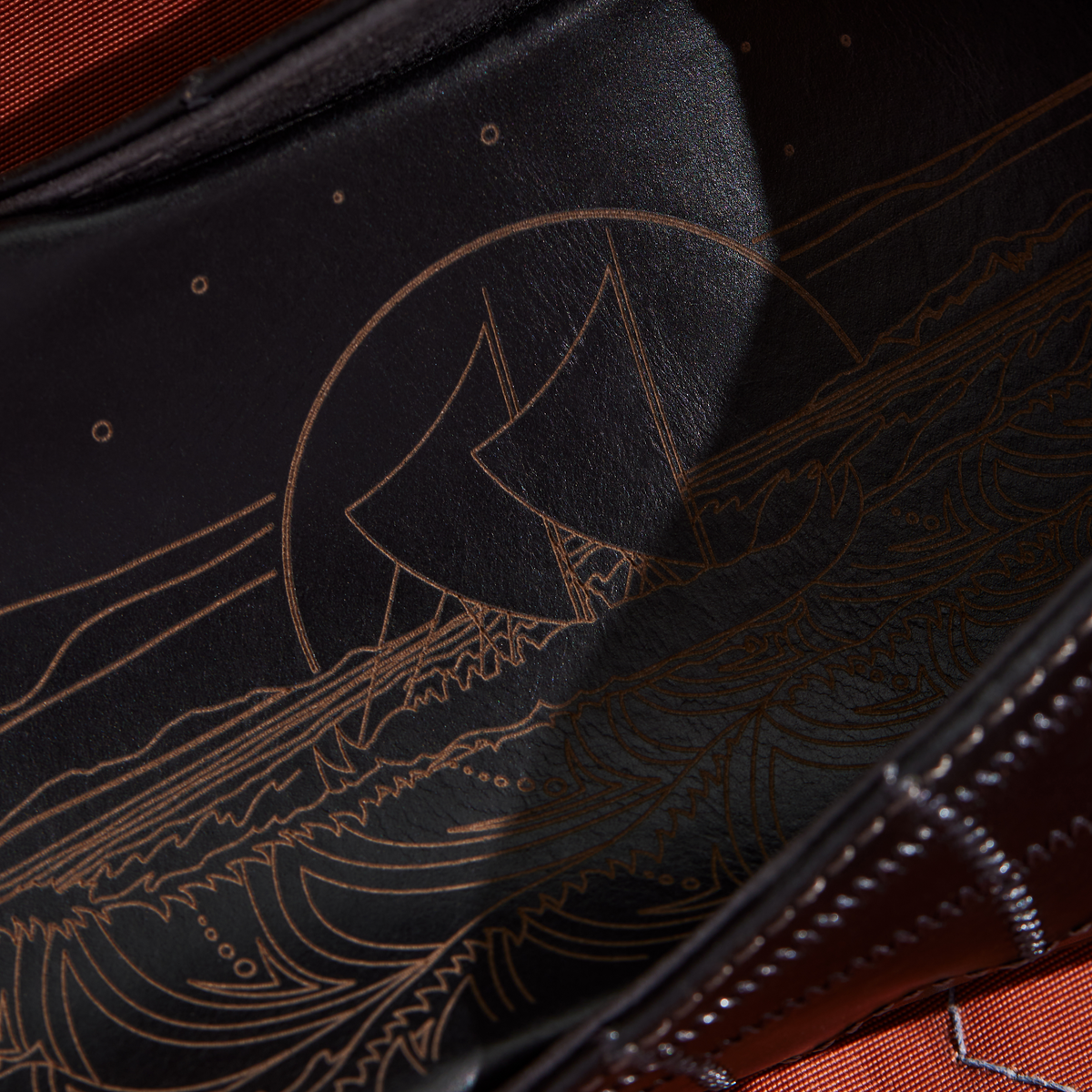 Black cap with copper-colored embroidered design featuring a stylized sailing canoe and decorative patterns.